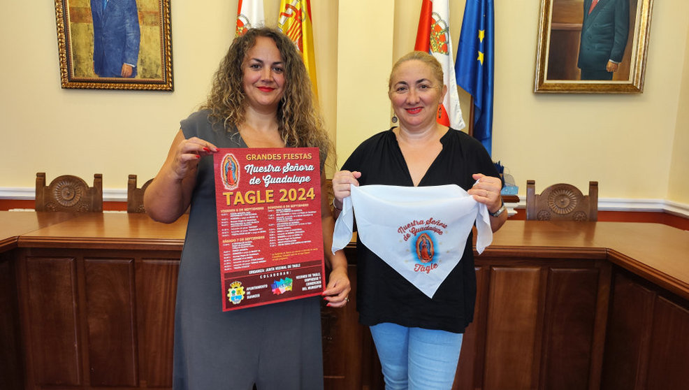 La concejala Raquel Fernández y la presidenta de la Junta Vecinal, Rebeca Pernía, con el cartel y el pañuelo de las fiestas de Guadalupe