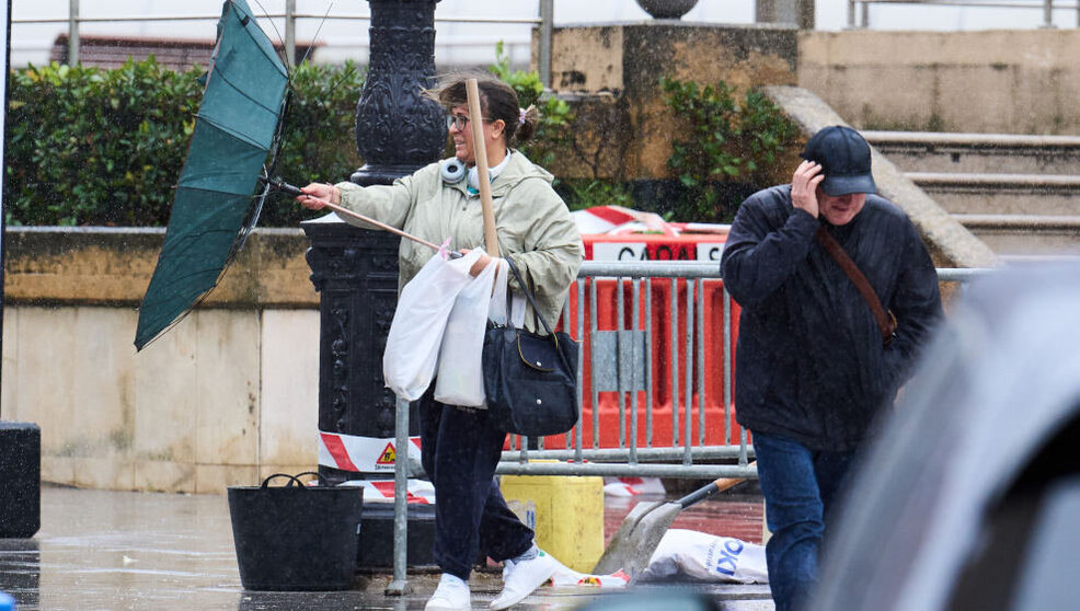 Varias personas tratan de cubrirse de la lluvia y el viento,