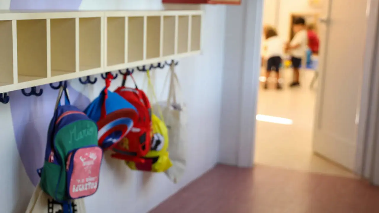 Varias mochilas en una percha de un aula de un colegio