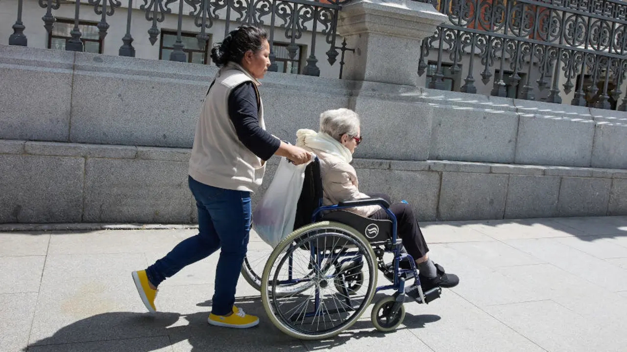 Mujer mayor en silla de ruedas y su cuidadora paseando