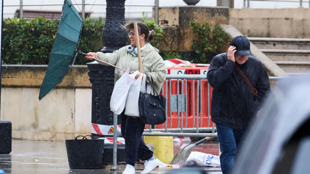 Varias personas tratan de cubrirse de la lluvia y el viento,